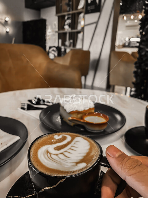 صورة لطاولة عليها مشروب الكابتشينو اللذيذ الساخن وطبق من الحلويات الشهية ، أجواء رائعة وجميلة في متجر القهوة بالمملكة العربية السعودية ، أماكن سياحية في السعودية ، مقهى سعودي