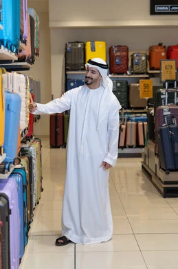 رجل إماراتي بالزي التقليدي يتسوق لشراء حقائب السفر