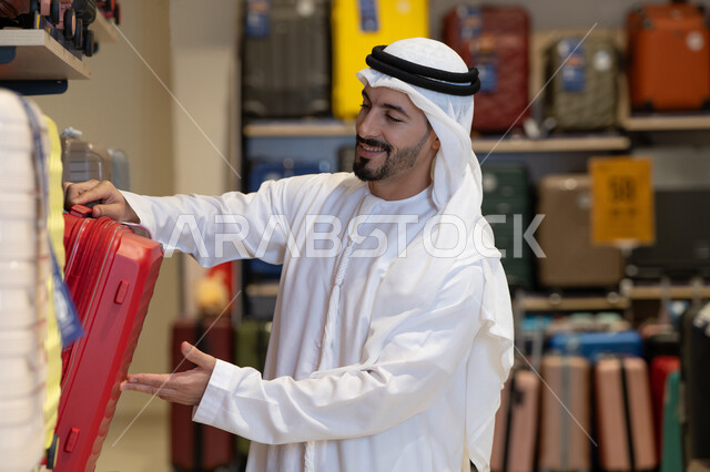 رجل إماراتي يتسوق لشراء حقيبة سفر حمراء في متجر