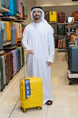 رجل إماراتي مع حقيبة سفر صفراء في متجر حقائب