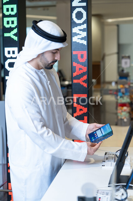 رجل إماراتي بالكندورة يتسوق للهواتف الذكية في المتجر