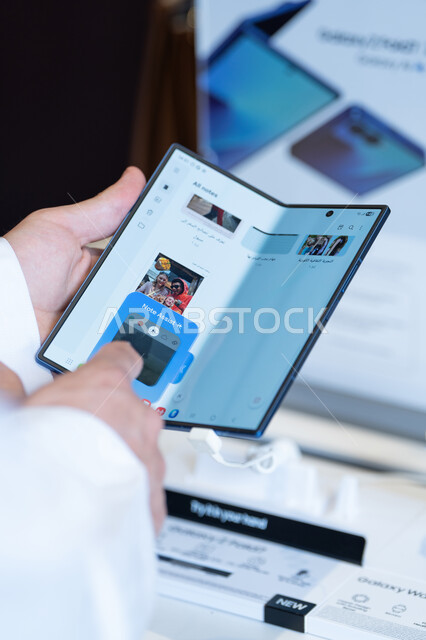 رجل سعودي بالثوب يستخدم هاتف ذكي قابل للطي