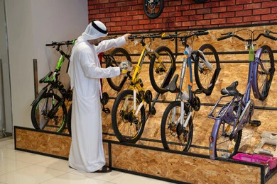رجل إماراتي بالكندورة يتسوق في محل دراجات هوائية