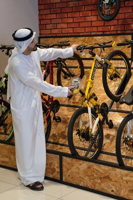 رجل إماراتي بالكندورة يتفحص دراجة في متجر