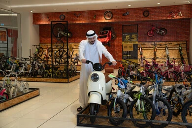 رجل إماراتي مع سكوتر في محل دراجات حديث