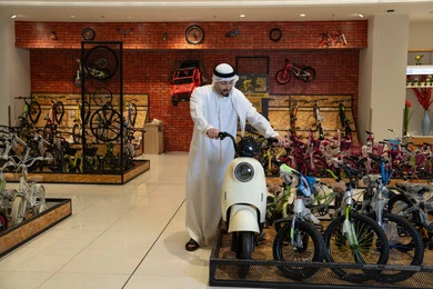 رجل إماراتي بالكندورة يتفقد سكوتر في محل دراجات