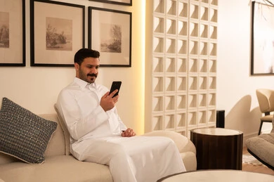 Saudi Man in Thobe Using Smartphone on Sofa