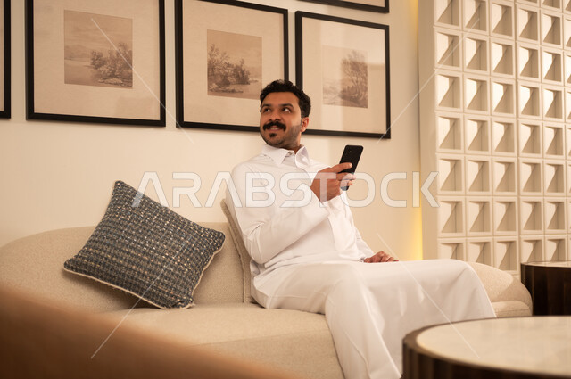 Saudi Man Using Smartphone on Sofa in Modern Living Room