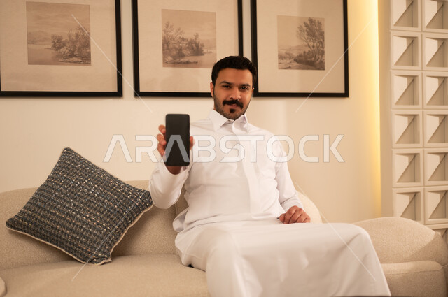 رجل سعودي بالثوب يحمل هاتف ذكي بشاشة فارغة