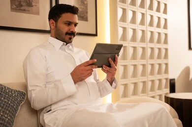 رجل سعودي بالثوب الأبيض يستخدم جهاز لوحي