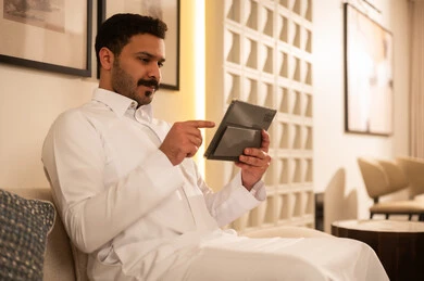رجل سعودي بالثوب الأبيض يستخدم جهاز لوحي في المنزل