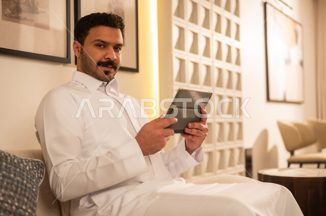 رجل سعودي مع جهاز لوحي في غرفة معيشة عصرية