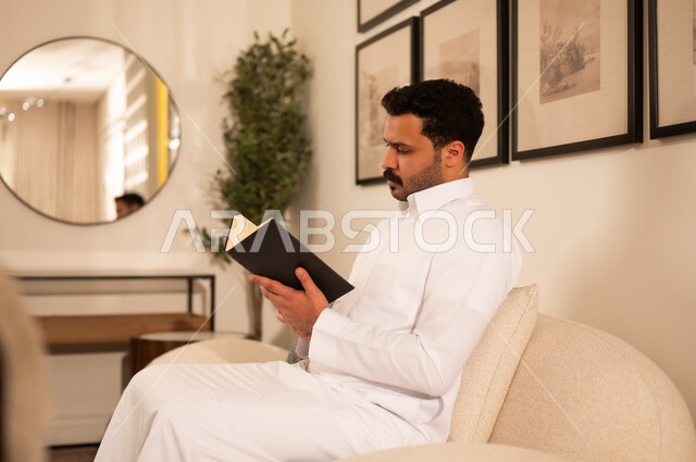 رجل عربي بالثوب الأبيض يقرأ كتاباً في الداخل
