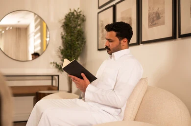 رجل عربي بالثوب الأبيض يقرأ كتاباً في الداخل