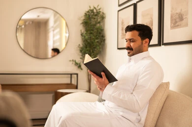 رجل سعودي بالثوب التقليدي يقرأ كتاباً في منزل عصري