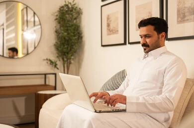 رجل سعودي يستخدم اللابتوب في غرفة معيشة حديثة رجل سعودي يستخدم اللابتوب في غرفة معيشة حديثة