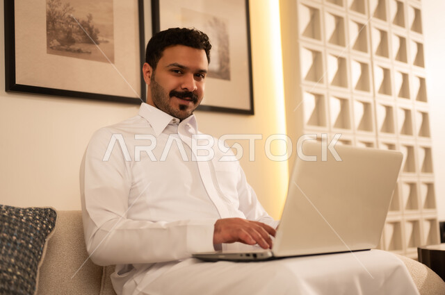 رجل سعودي بالثوب التقليدي يستخدم جهاز كمبيوتر محمول
