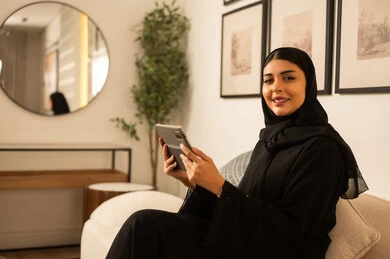 امرأة سعودية مع جهاز لوحي في غرفة معيشة حديثة