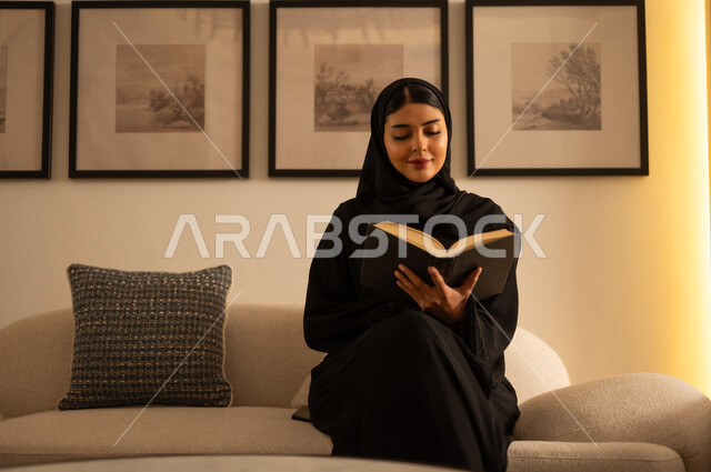 امرأة سعودية بالعباءة تقرأ كتاباً على الأريكة