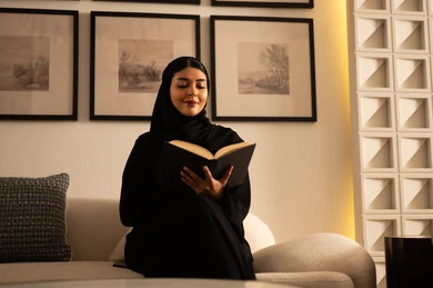 امرأة سعودية بالعباءة تقرأ كتاباً في المنزل