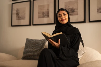 امرأة سعودية تقرأ كتاباً على الأريكة في المنزل