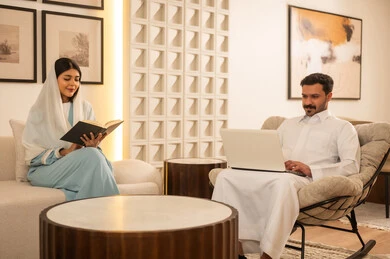 Saudi Couple Using Laptop and Reading in Modern Living Room