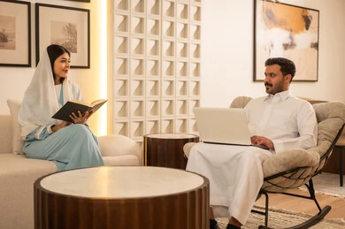 زوجين سعوديين يستخدمان اللابتوب والقراءة في منزل حديث