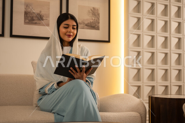 امرأة عربية تقرأ كتاباً في غرفة معيشة داخلية حديثة