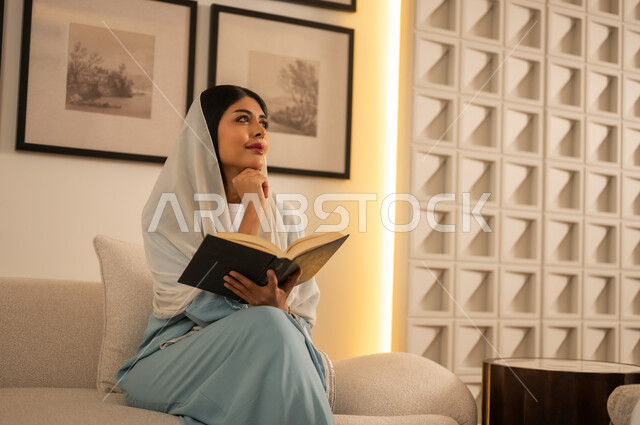 امرأة سعودية تقرأ كتاباً في غرفة معيشة حديثة