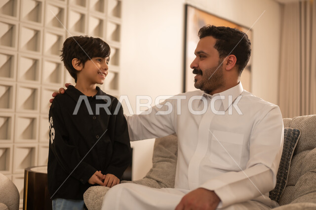 أب سعودي يبتسم لابنه في غرفة معيشة حديثة بإضاءة دافئة
