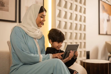 أم عربية وابنها يستخدمان الجهاز اللوحي في غرفة المعيشة أم عربية وابنها يستخدمان الجهاز اللوحي في غرفة المعيشة