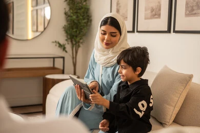 أم عربية وابنها يستخدمان الجهاز اللوحي في غرفة المعيشة