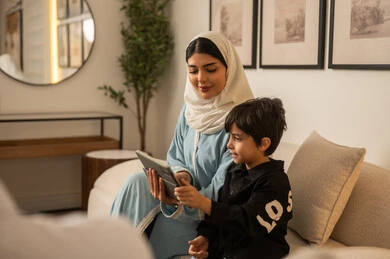 امرأة عربية وطفل يستخدمان الجهاز اللوحي في المنزل