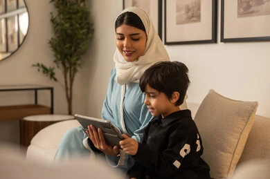 أم سعودية وابنها يستخدمان الجهاز اللوحي في المنزل