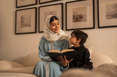 أم عربية تقرأ كتاباً مع ابنها في غرفة المعيشة