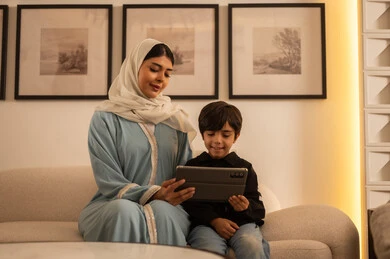 أم عربية وابنها يستخدمان جهاز لوحي في غرفة المعيشة