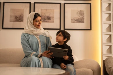 امرأة عربية وطفل مع جهاز لوحي في غرفة معيشة عصرية