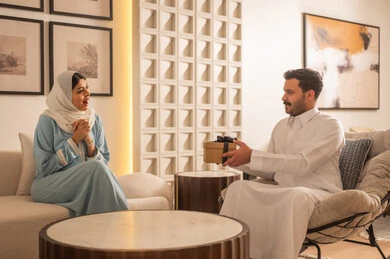 رجل سعودي يقدم هدية لامرأة في غرفة معيشة عصرية