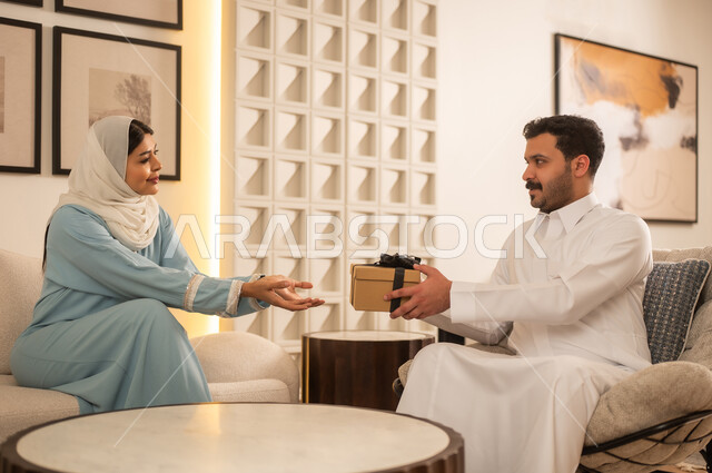 رجل سعودي يقدم هدية لامرأة في غرفة معيشة عصرية
