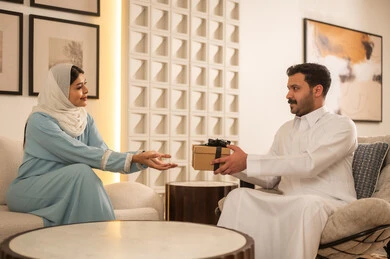 رجل سعودي يقدم هدية لامرأة في غرفة معيشة عصرية