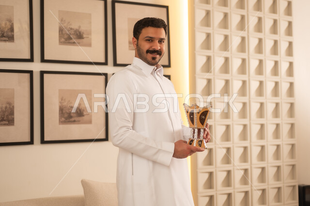 رجل سعودي يرتدي الثوب يحمل مبخرة تقليدية في الداخل