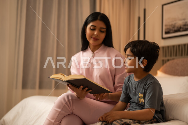 أم عربية تقرأ كتاباً لابنها الصغير في المنزل
