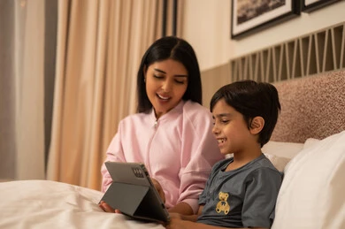 أم عربية وابنها يستخدمان الجهاز اللوحي في غرفة النوم