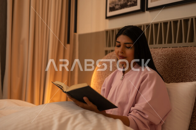 امرأة شابة تقرأ كتاباً في السرير بإضاءة دافئة