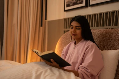 Young Woman Reading Book in Bed with Warm Lighting