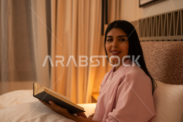 امرأة عربية تقرأ كتابا في السرير بإضاءة دافئة