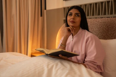 Arab Woman Reading Book in Bedroom Under Warm Light