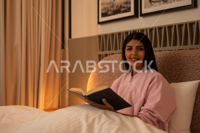 امرأة عربية تقرأ كتاباً في السرير بإضاءة دافئة