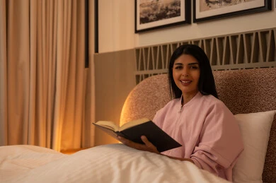 امرأة عربية تقرأ كتاباً في السرير بإضاءة دافئة