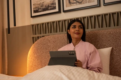 امرأة عربية تستخدم جهازاً لوحياً في غرفة نوم حديثة ليلاً